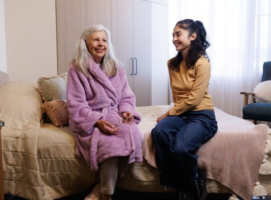 A woman and a carer sitting on a bed at HammondCare Caulfield residential aged care in Melbourne